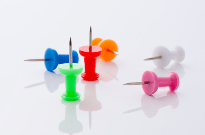 different colored thumbtacks on white background